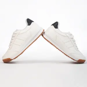 Tenis urbanos color crema con suela de goma color caramelo y detalle negro en el talón, mostrados de perfil en ángulo sobre fondo blanco.